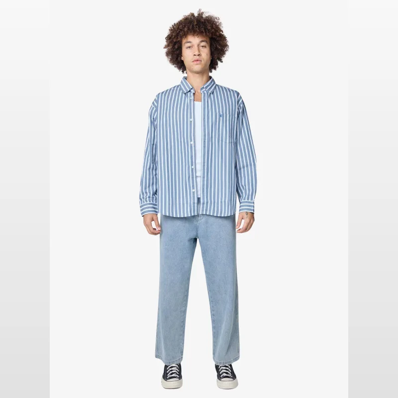 Man wearing a blue and white striped long sleeve shirt with a chest pocket and embroidered 'C' logo, paired with light wash jeans.