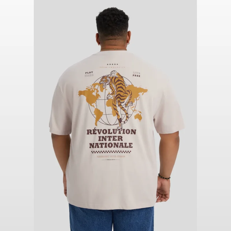 Back view of a man wearing a putty-coloured, relaxed fit t-shirt with a graphic print of a tiger on a world map and text 'REVOLUTION INTER NATIONALE'.