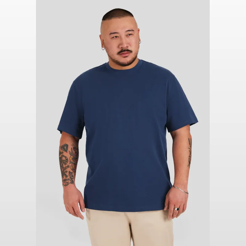 Man wearing a dark indigo blue classic heavy weight t-shirt with a crew neck and short sleeves, paired with light beige trousers.
