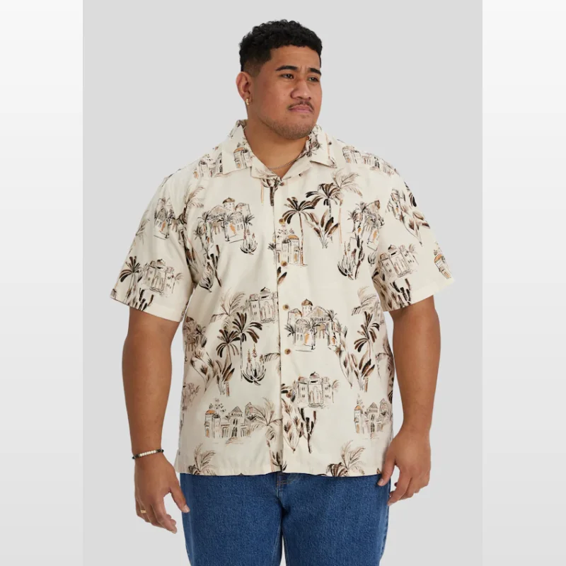 Man wearing an ECRU CASABLANCA RELAXED FIT SHIRT by Johnny Bigg, featuring a relaxed fit, cuban collar, and a print of buildings and palm trees.
