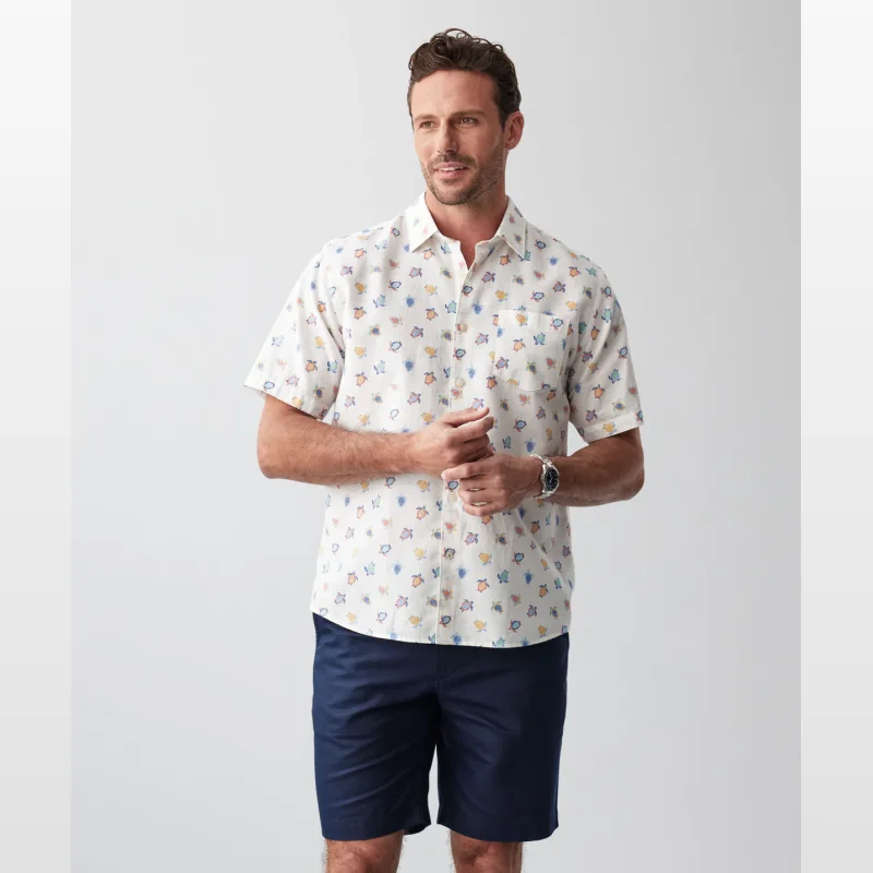 Man wearing a cream short sleeve shirt with a colourful turtle print and navy shorts.