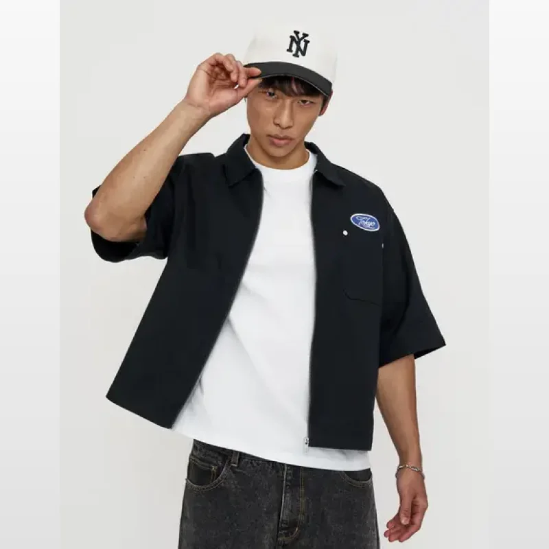 Man wearing a black short-sleeved mechanic zip-up shirt with a white t-shirt underneath and a Tokyo patch on the chest.
