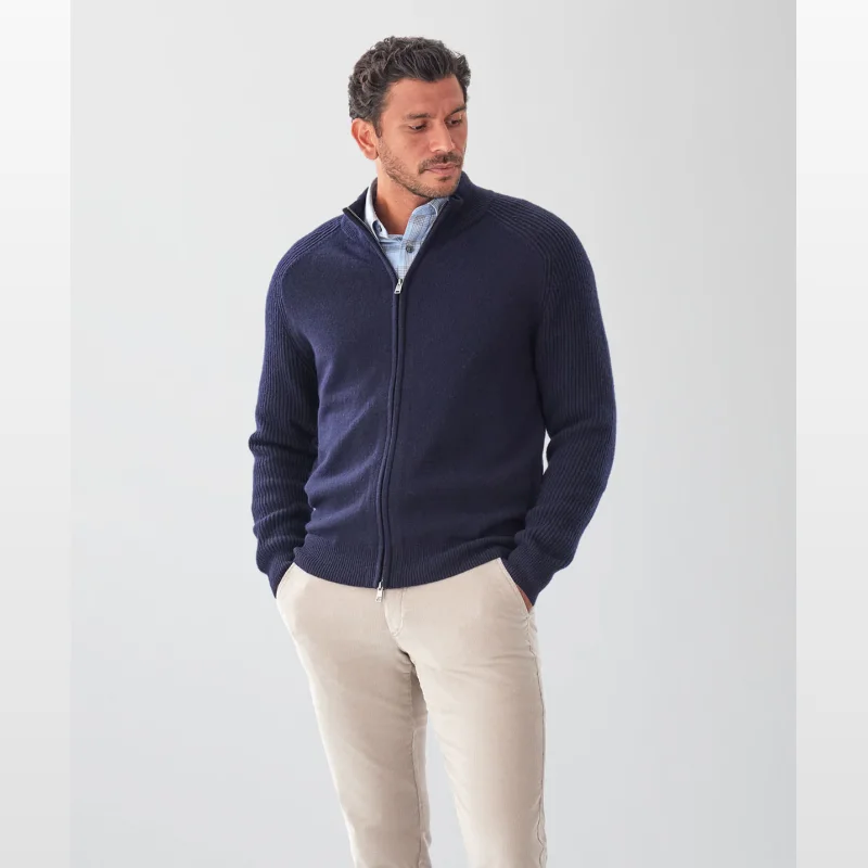 Man wearing a navy blue wool blend raglan zip cardigan with a funnel neck and beige trousers.