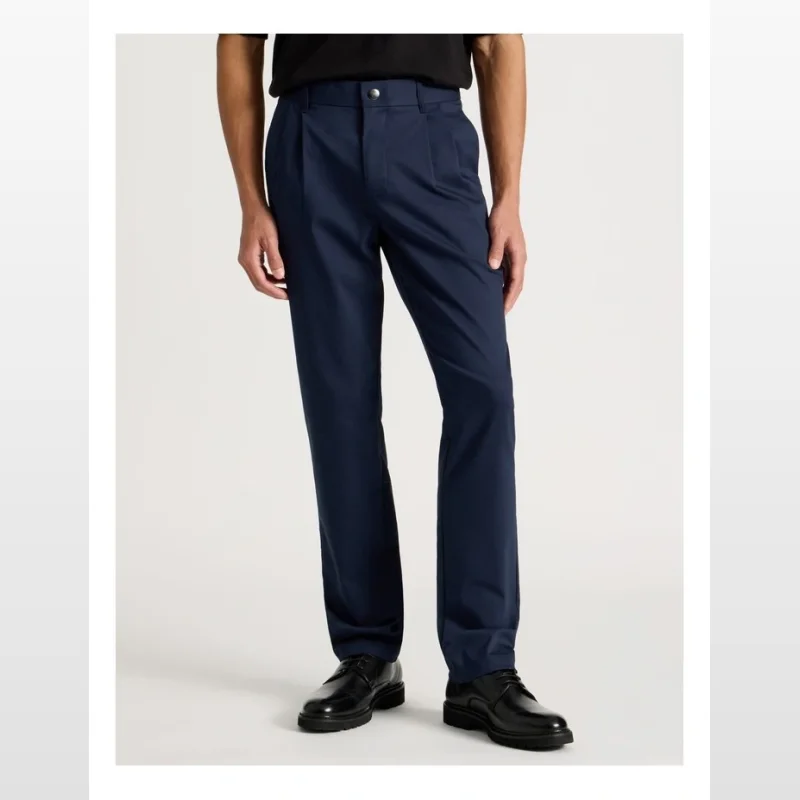 A man wearing navy blue pleated relaxed fit trousers and black dress shoes.