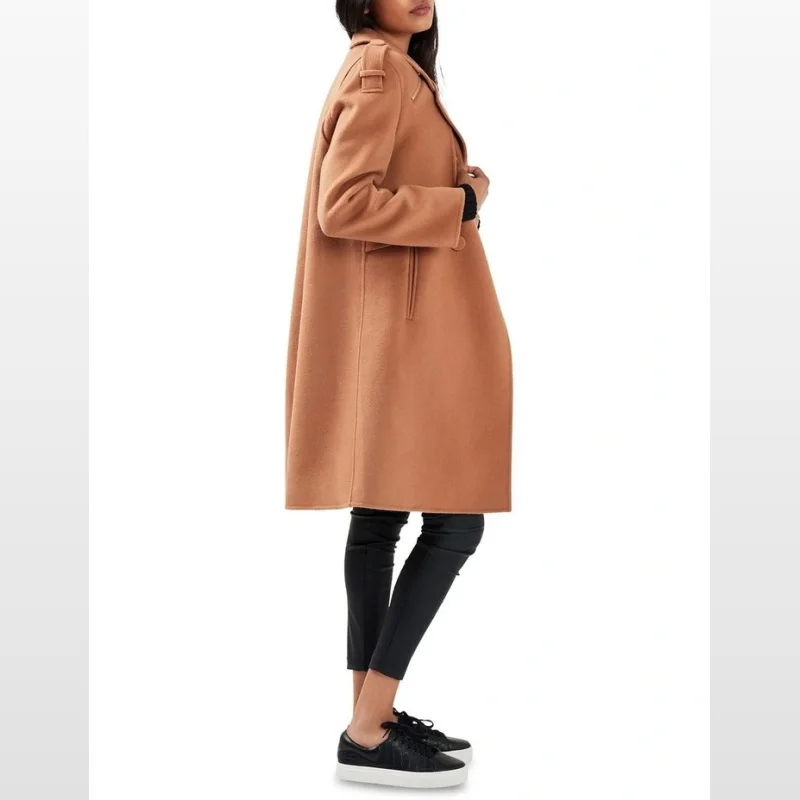 Woman wearing a camel-coloured wool blend double-breasted coat with notched lapels and epaulettes, paired with black leggings and sneakers.