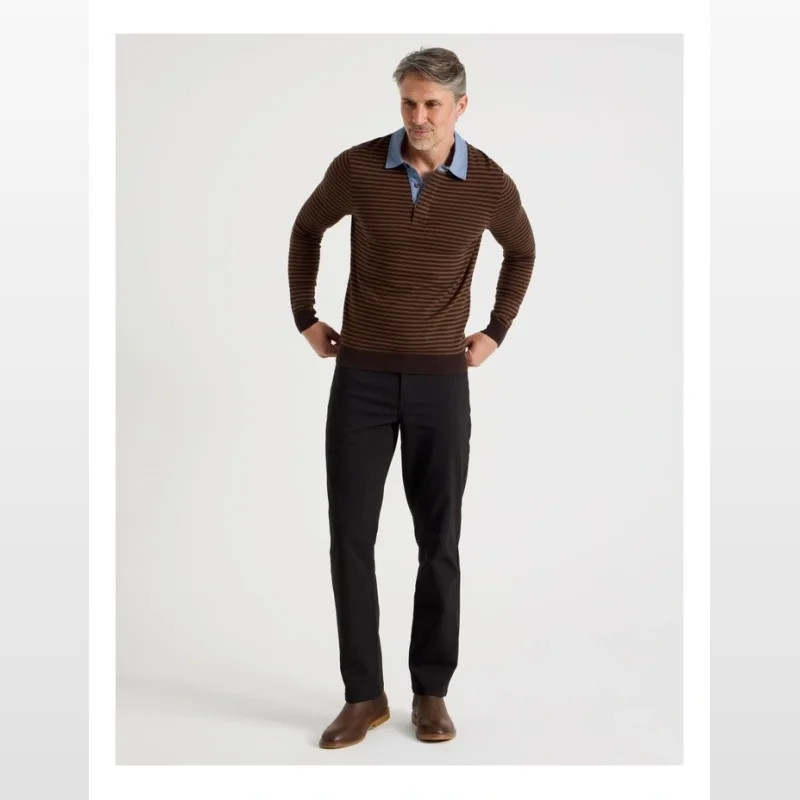 Man wearing a brown and dark brown striped knitted long-sleeve rugby polo shirt with a light blue collar, paired with black trousers and brown boots.