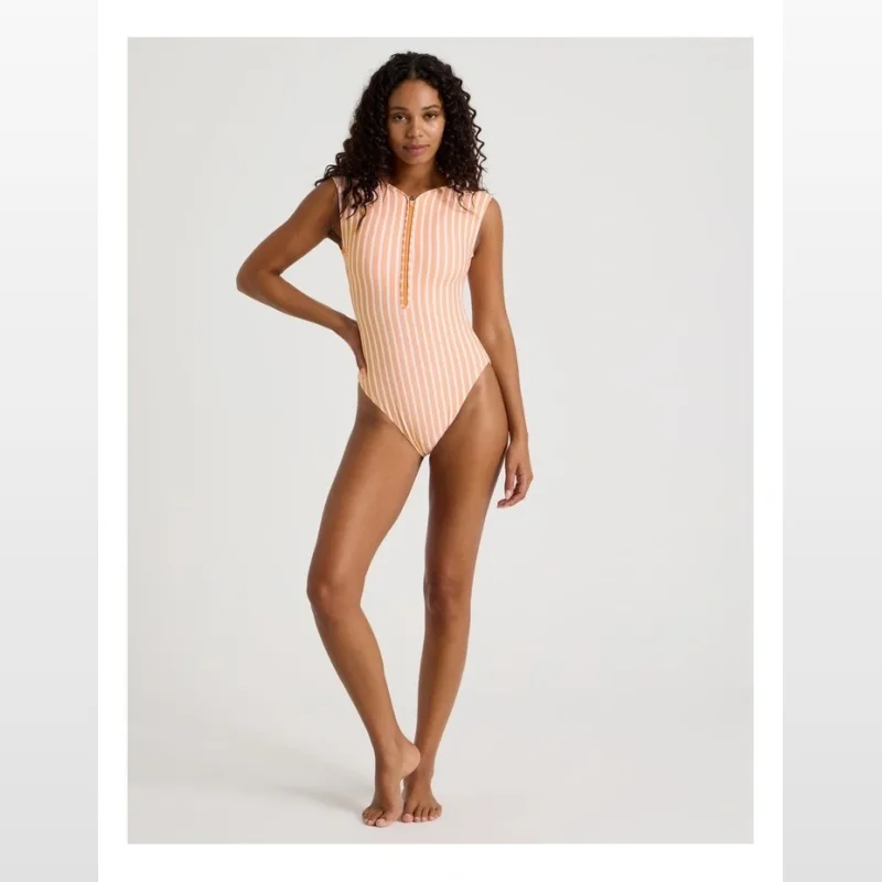 Woman wearing a peach and white striped one-piece swimsuit with a zip front.