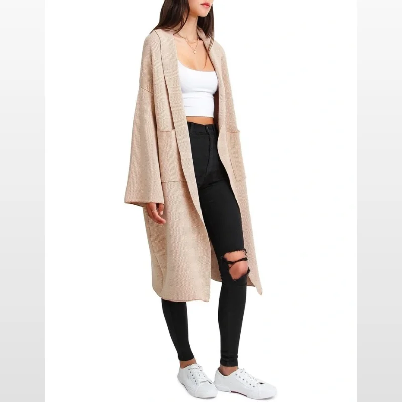 Woman wearing a beige, long-sleeved coatigan with a herringbone pattern, shawl collar, and patch pockets, paired with a white crop top and black ripped jeans.