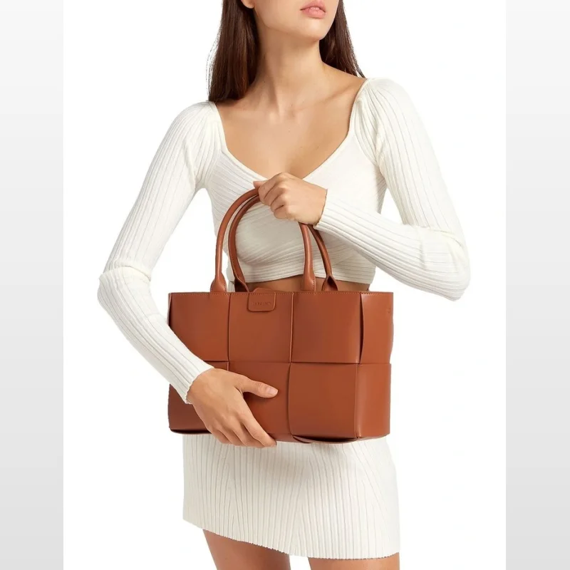 Woman holding a brown woven genuine leather tote bag with gold hardware.