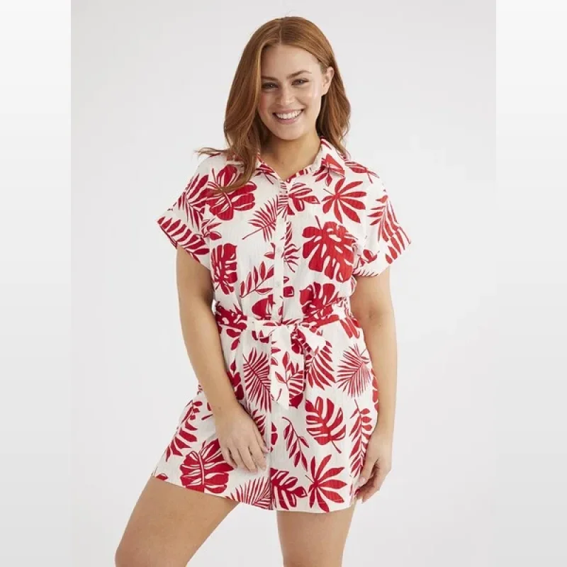 Woman wearing a cream short-sleeve playsuit with a red palm leaf print, featuring a button-up front, open collar, and a tie waist.