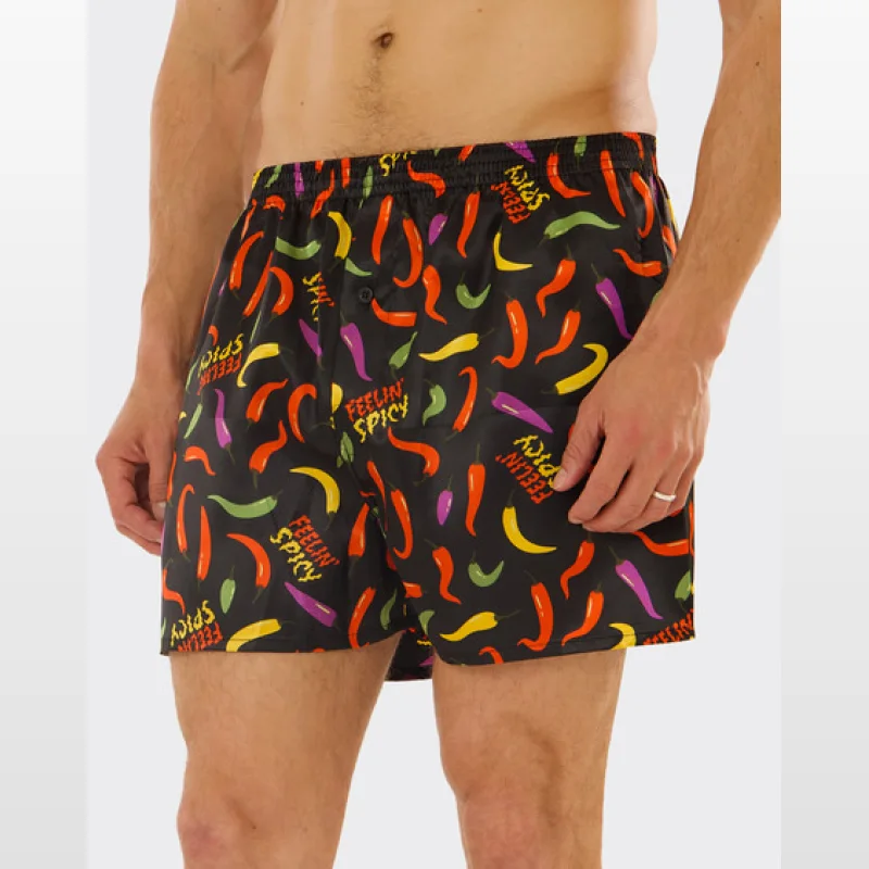 Close-up of a man wearing black satin boxer shorts with a repeating print of colourful chilli peppers and the text 'Feelin' Spicy'.