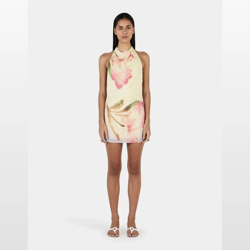 Woman wearing the Ownley Louisa Mini Dress, a pale yellow dress with a large pink floral print, featuring a high cowl neck and a backless design with an adjustable strap.