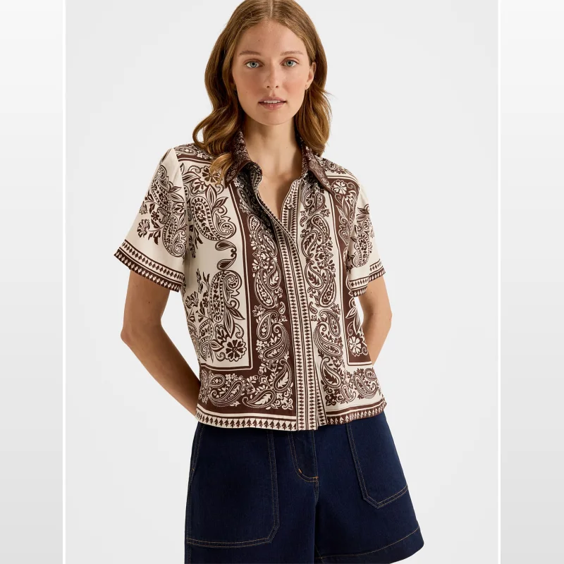 Woman wearing a brown and cream paisley print short-sleeve cropped shirt with a relaxed fit.