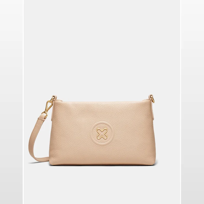 A light beige Mimco Bay Strap Crossbody Bag made of pebbled leather with a gold-toned logo emblem and a detachable crossbody strap.