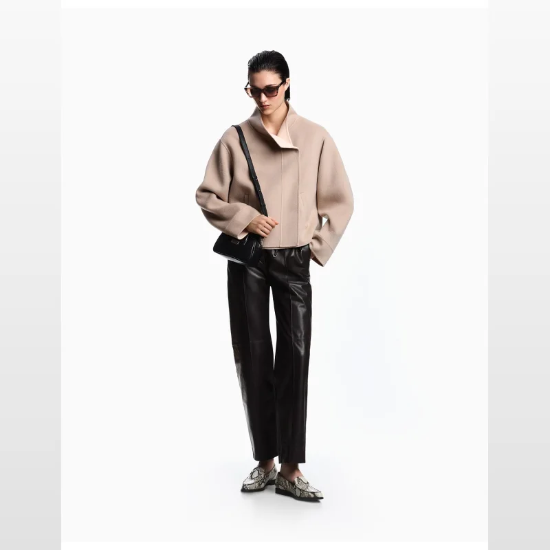 Woman wearing black Emporio Armani lamb leather trousers and a beige jacket, holding a black handbag.
