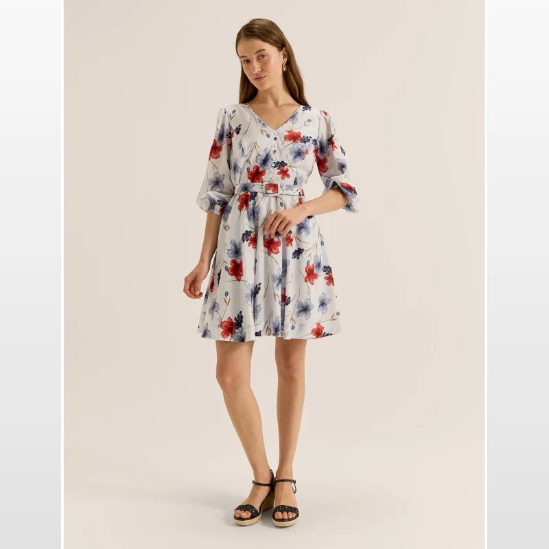 Woman wearing the REVIEW Rosa Mini Dress, a white dress with a muted red and blue floral print, a V-neck, three-quarter sleeves, and a matching belt.