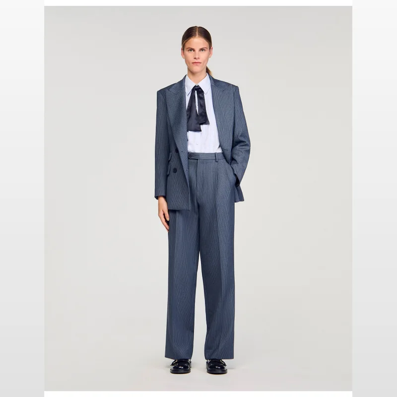 Woman wearing Sandro Paris Naelo wide-leg striped trousers with a matching blazer, white shirt, and black bow tie.
