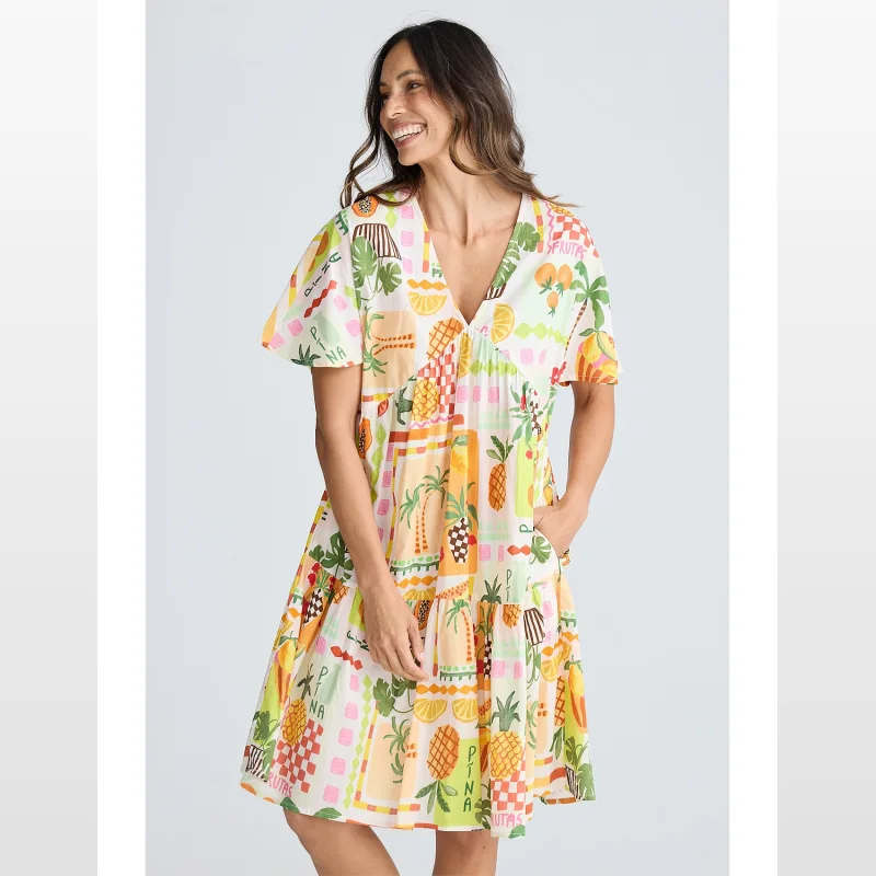 Woman wearing a short-sleeved, V-neck, tiered mini dress with a colourful tropical fruit and palm tree print.