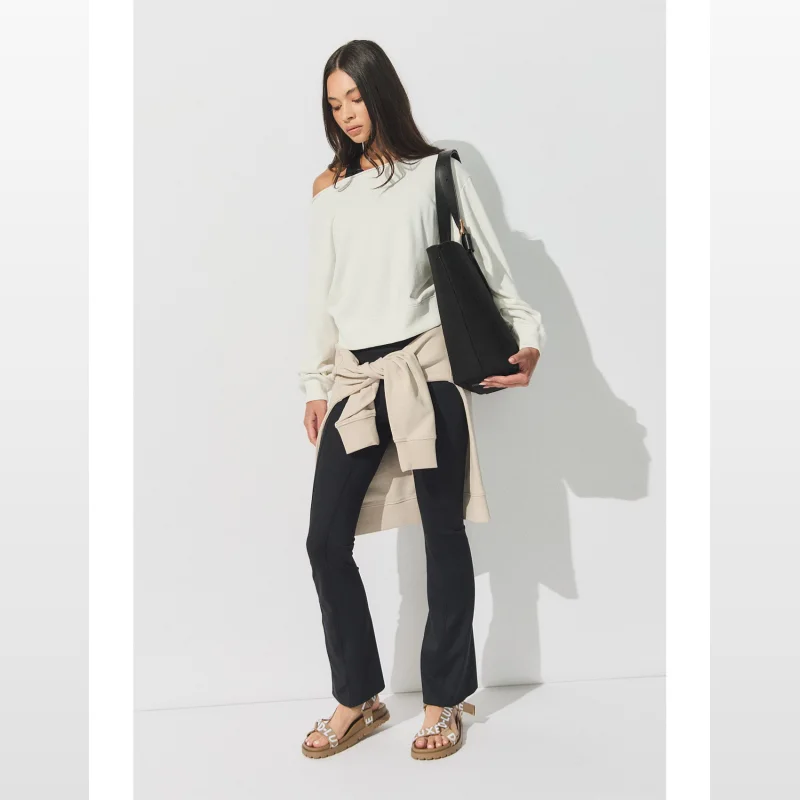 Model wearing black DECJUBA D-LUXE Yoga Flare Leggings with a cream off-the-shoulder top and a beige cardigan tied around her waist.