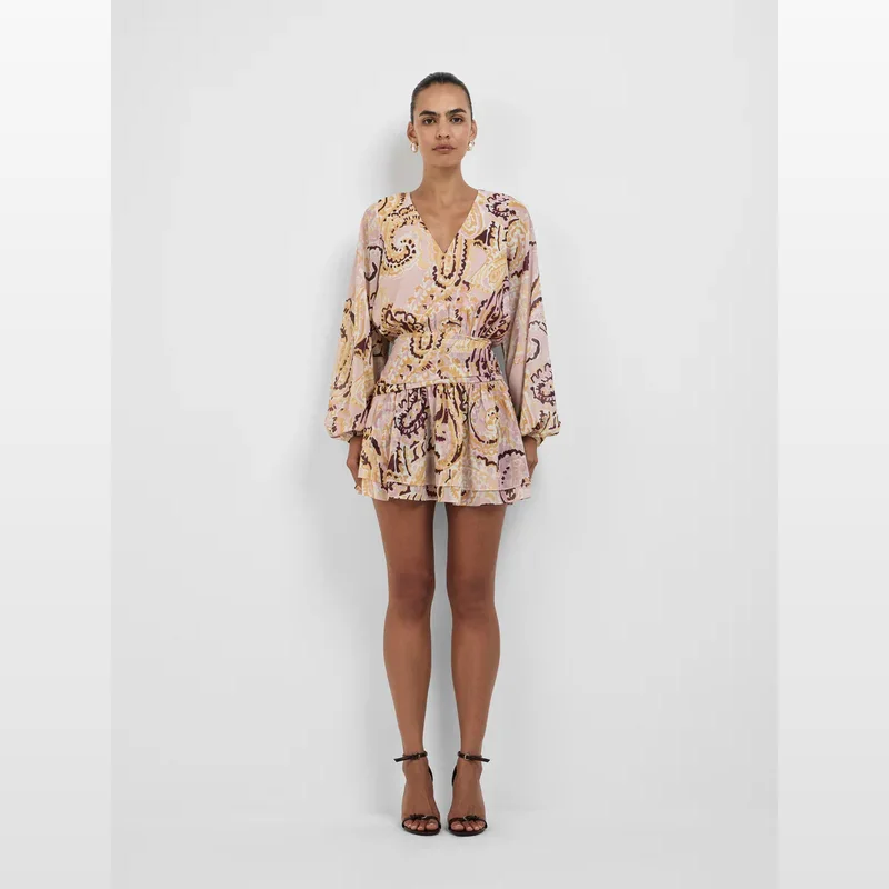 Woman wearing the Sheike Leona Mini Dress, a pink and yellow paisley print mini dress with long sleeves and a V-neck.