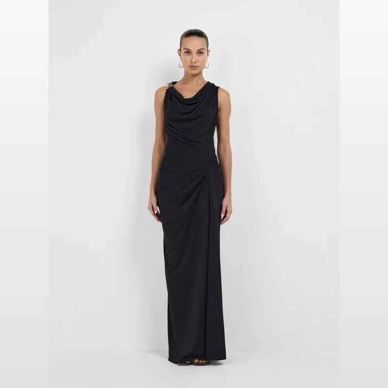 Woman wearing the Sheike Sorella Maxi Dress in black, featuring a cowl neckline with gold hardware detail on the shoulder, a fitted bodice with tuck detail, and a ruched maxi-length skirt.