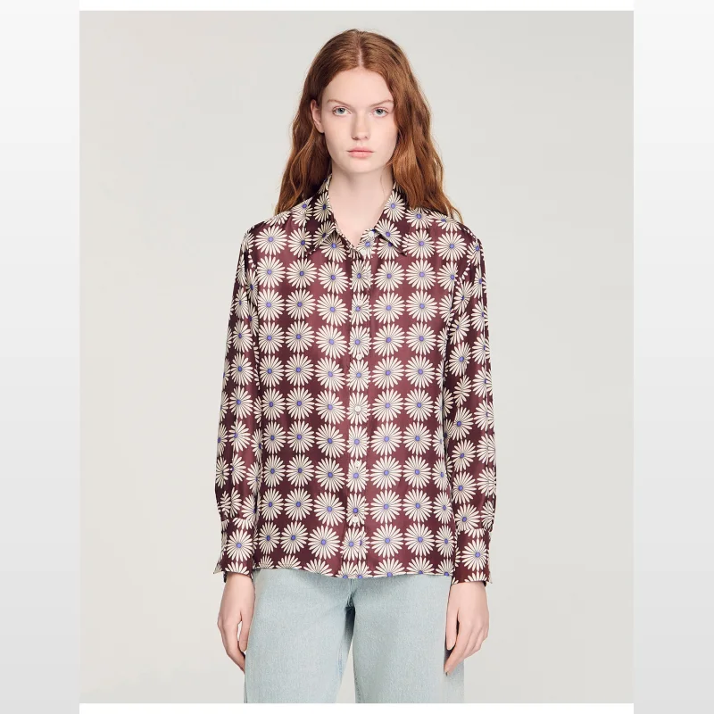 Woman wearing a Sandro Paris Dorina floral print silk shirt with a shirt collar, long sleeves, and buttoned cuffs.