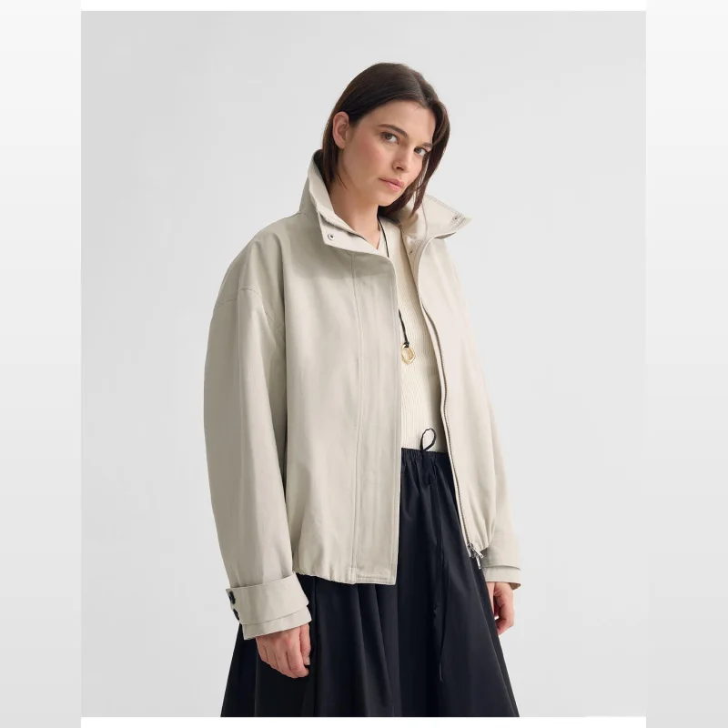 Woman wearing an oversized, mid-length beige cotton bomber jacket with a statement collar, zip front, cuff tabs, and elasticated waist.
