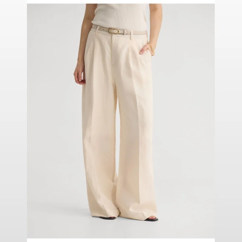 Woman wearing cream coloured wide leg trousers with a cream belt and a ribbed cream top.