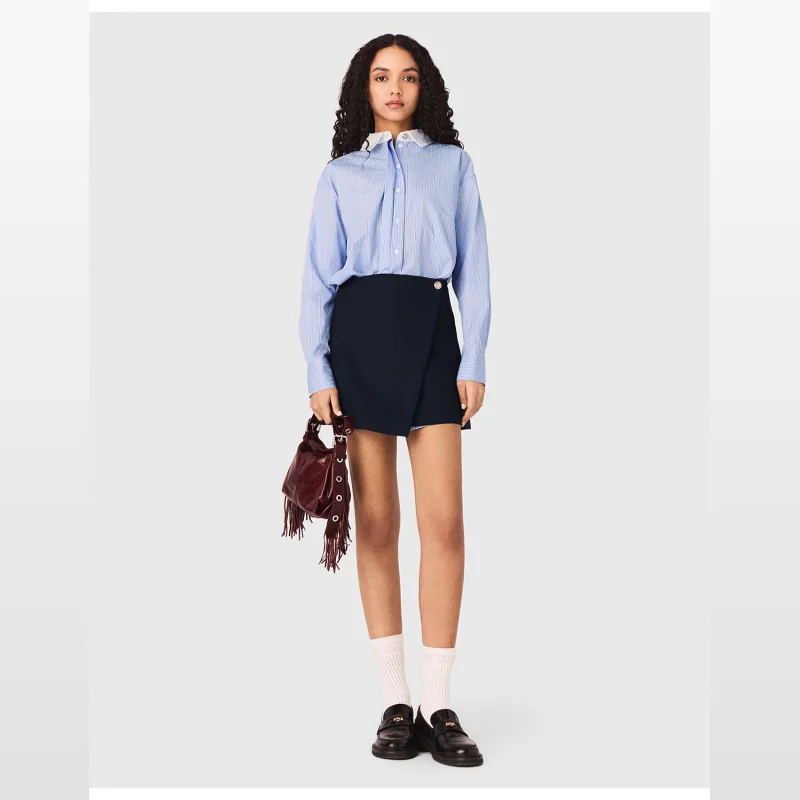 Model wearing a MAJE Riback Dress, a blue and white striped shirt dress with a navy blue asymmetrical wrap skirt and a white collar.