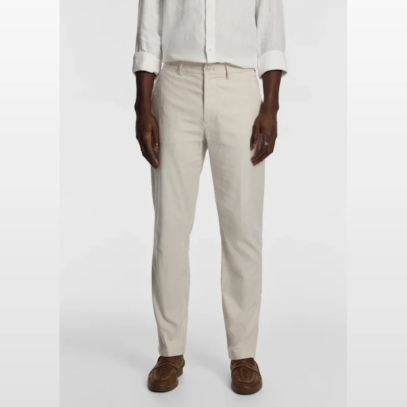 Man wearing natural coloured relaxed fit chino pants with a white linen shirt and brown woven loafers.