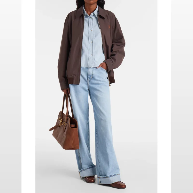 Model wearing FRAME DENIM The Cuffed Wide High Rise Wide Leg Jeans in a light blue wash, paired with a striped shirt and brown jacket.