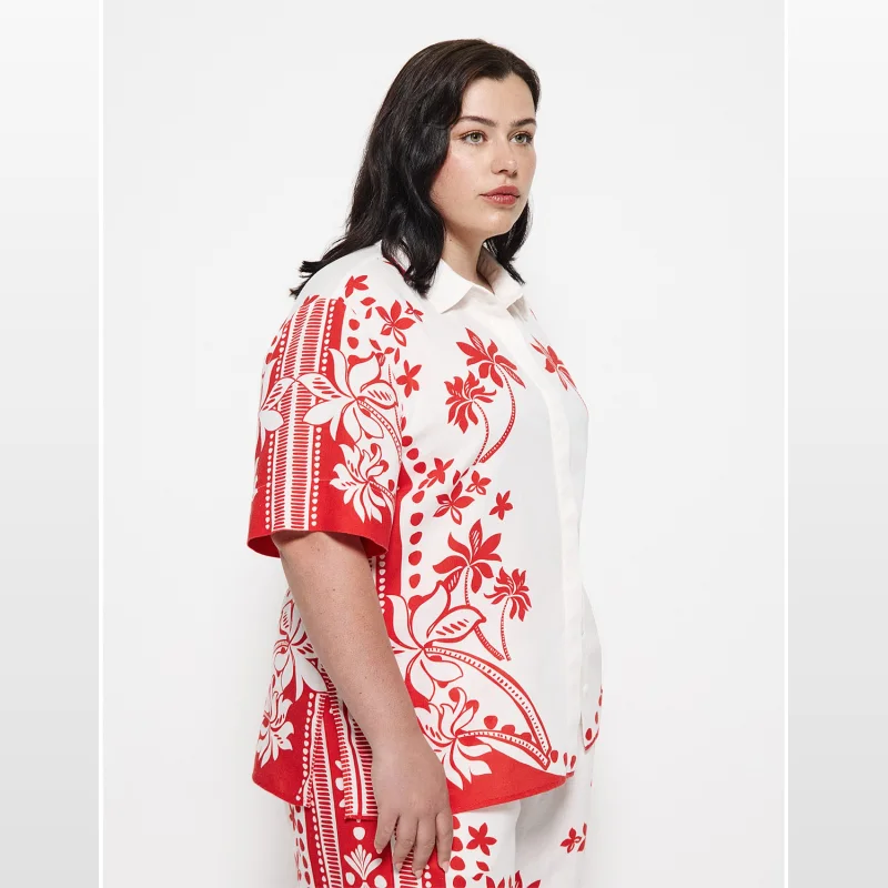 Woman wearing a white short-sleeved shirt with a bold red tropical palm print. The shirt has a concealed placket and a straight hem with side splits.