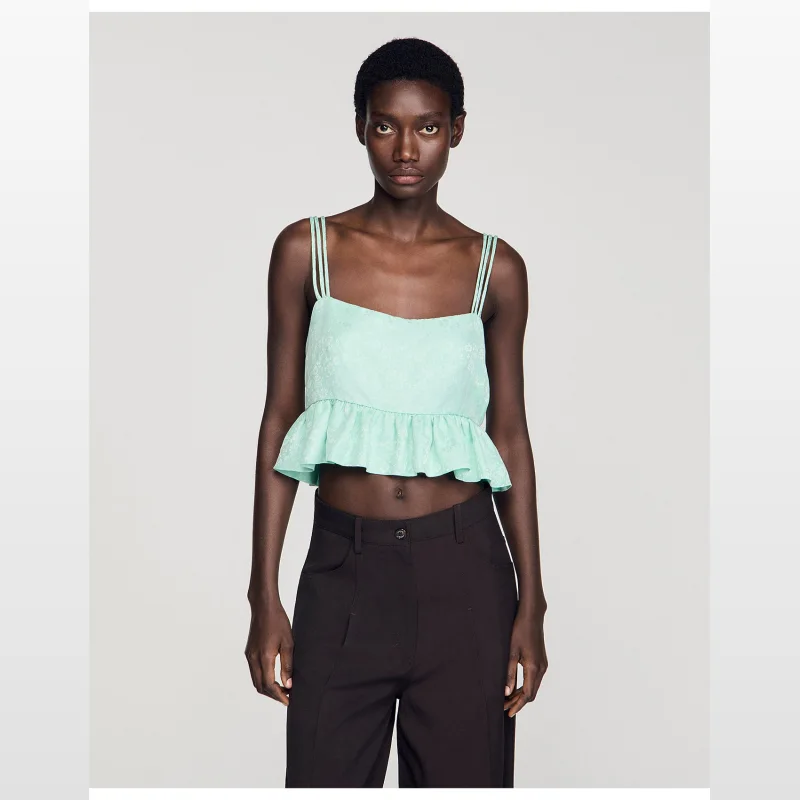 A woman wearing a mint green Sandro Paris Modie floral jacquard crop top with triple straps and a ruffled hem.