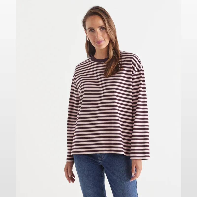 Woman wearing a plum and pink striped long sleeve oversized t-shirt with a crew neckline and blue denim jeans.