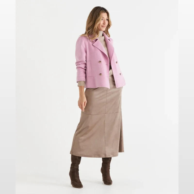 Woman wearing a taupe faux suede midi skirt with an A-line silhouette and side pockets, paired with a beige turtleneck and a pink double-breasted jacket.