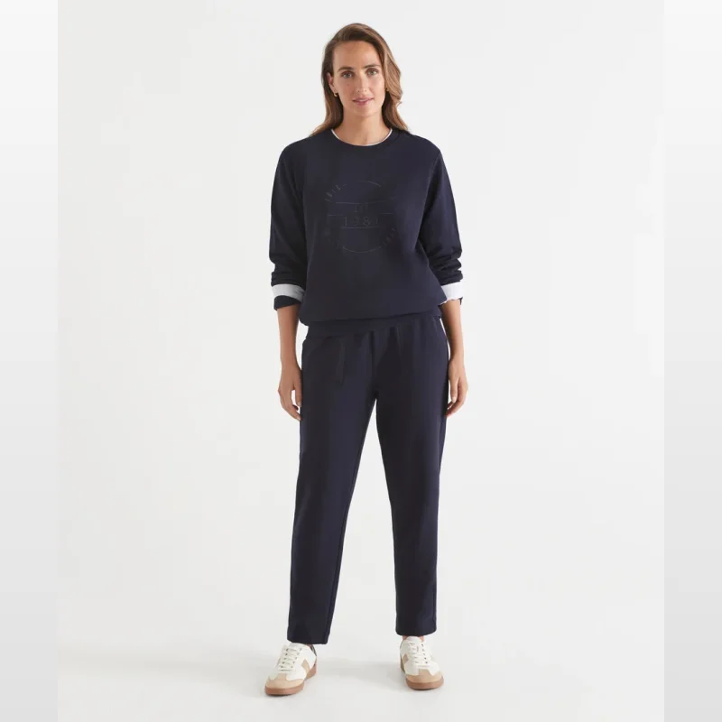 Woman wearing navy tapered leg joggers with an elastic waistband and pockets, paired with a matching navy sweatshirt and white sneakers.