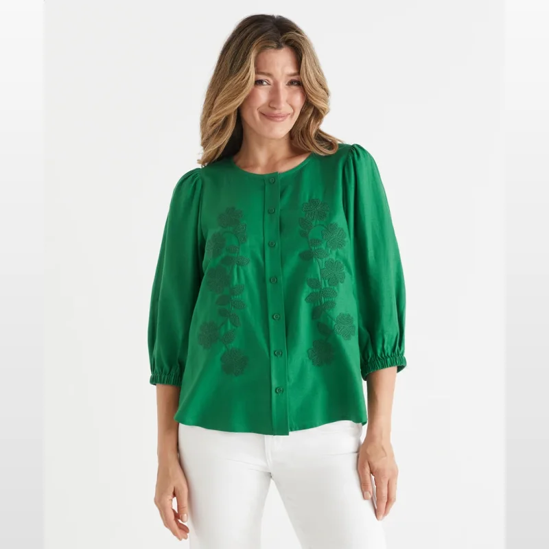 Woman wearing a green floral embroidered top with 3/4 sleeves and a scoop neckline.