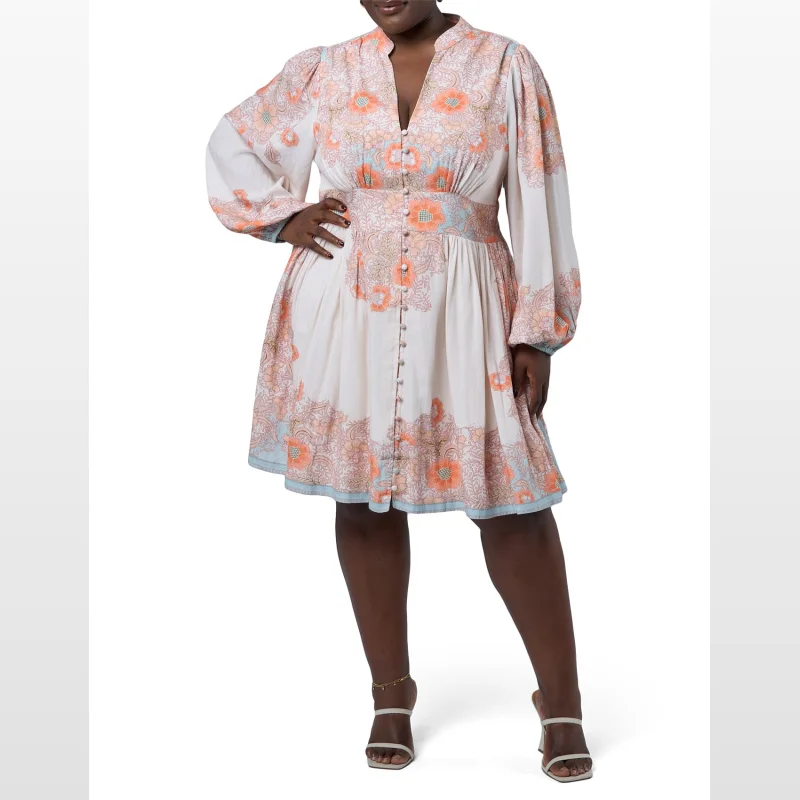 Plus size model wearing the Pink Dusk Virginia Mini Dress, a cream-coloured dress with a floral print in shades of pink, orange, and blue, featuring long sleeves, a V-neckline, and a button-down front.