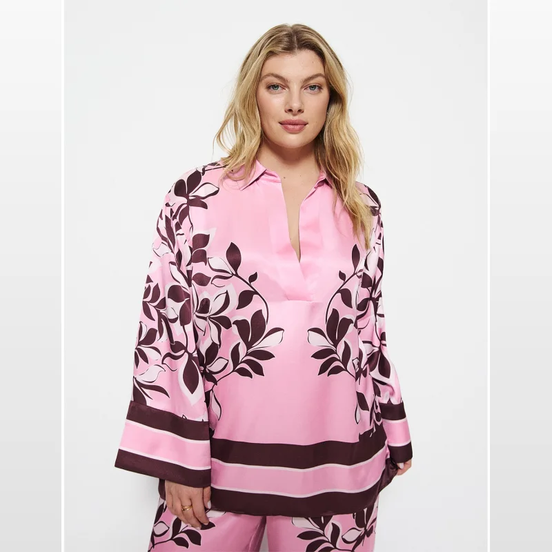 Woman wearing a pink satin top with a dark floral print and flared sleeves. The top has a V-neckline and side splits.