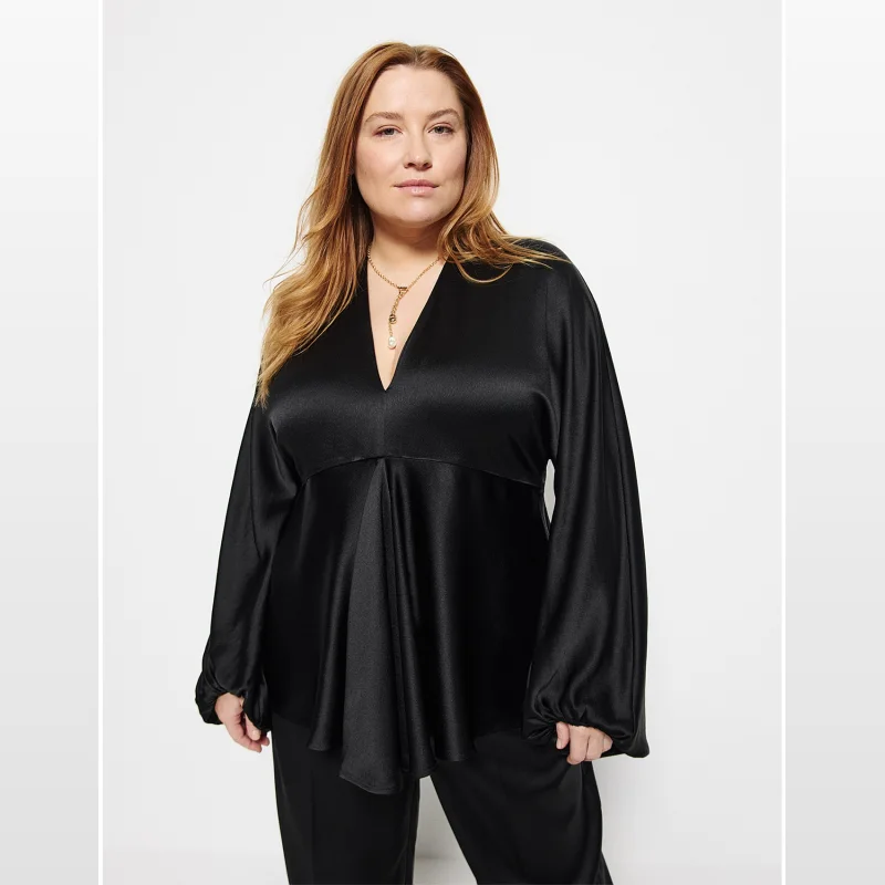 Woman wearing a black satin COMMONRY Julia Top with a plunging V-neckline and blouson sleeves.