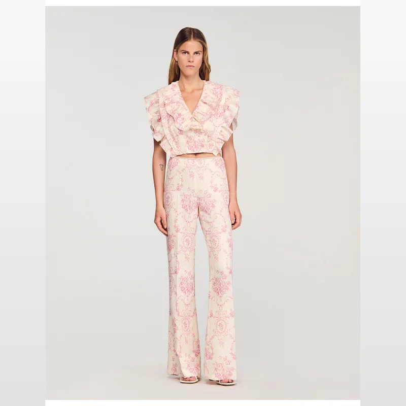 Woman wearing Sandro Paris Darwin trousers with a pink floral print and a matching ruffled top.