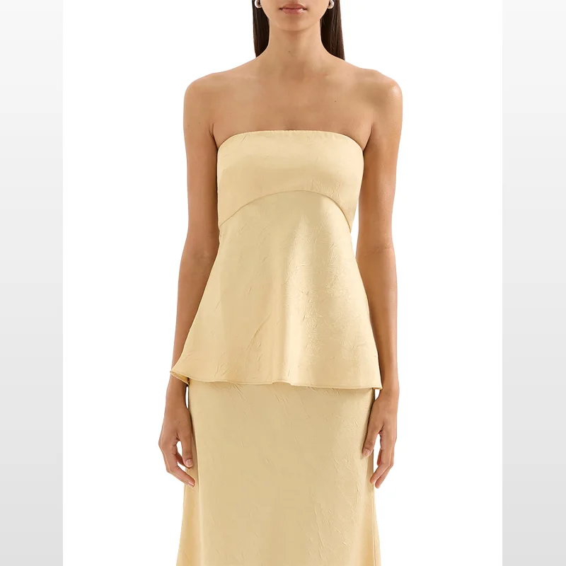 A woman wearing a pale yellow NUDE LUCY Pandora Strapless Top made of crushed satin with a fitted bust and a fluted hem.