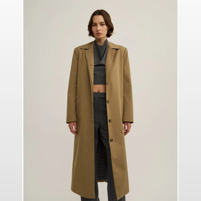 Model wearing a tan Witchery x Lara Worthington single-breasted trench coat over a grey top and trousers.