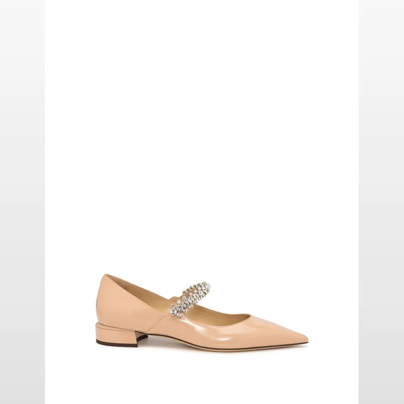 Close-up of a nude patent leather Jimmy Choo Bing Pump Flat shoe with a pointed toe, low block heel, and a strap embellished with sparkling crystals.