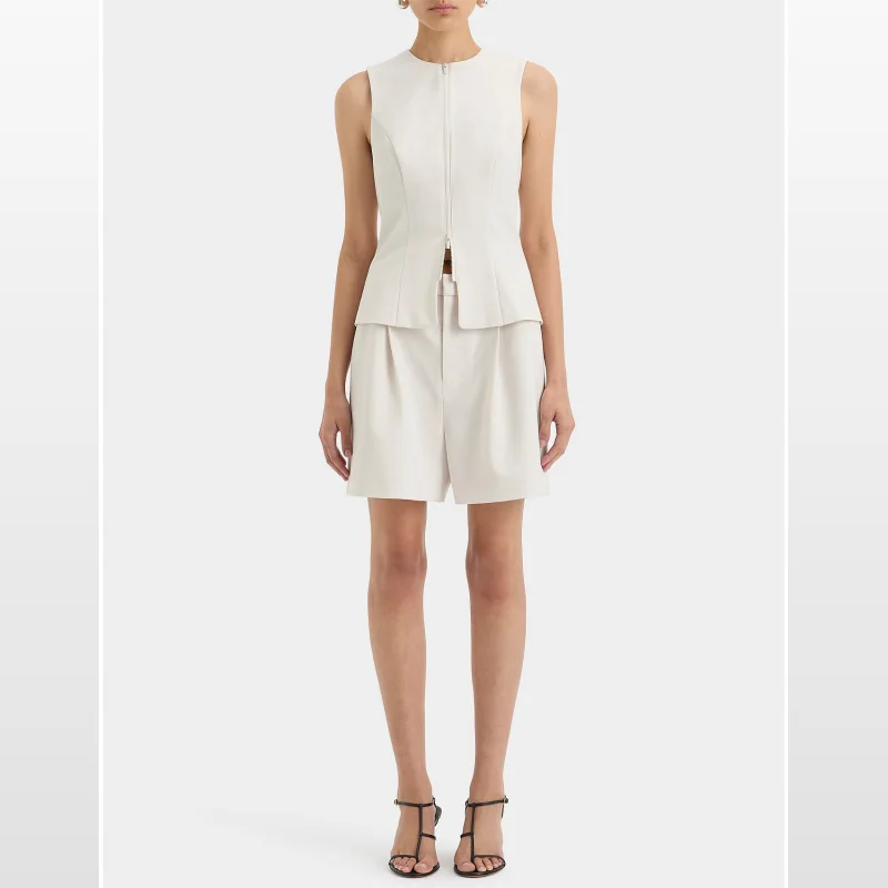 Model wearing white SIR Laredo tailored shorts with a pleated front, paired with a matching sleeveless zip-front top and black strappy heels.