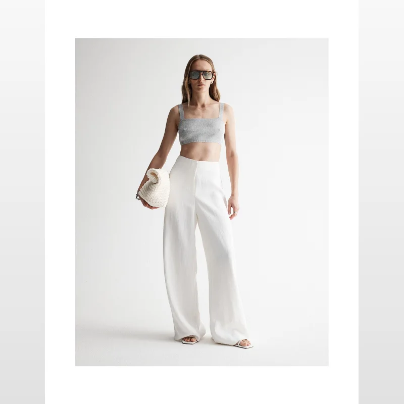 Woman wearing a grey ribbed knit bralette with a square neckline and wide shoulder straps, paired with white wide-leg pants.