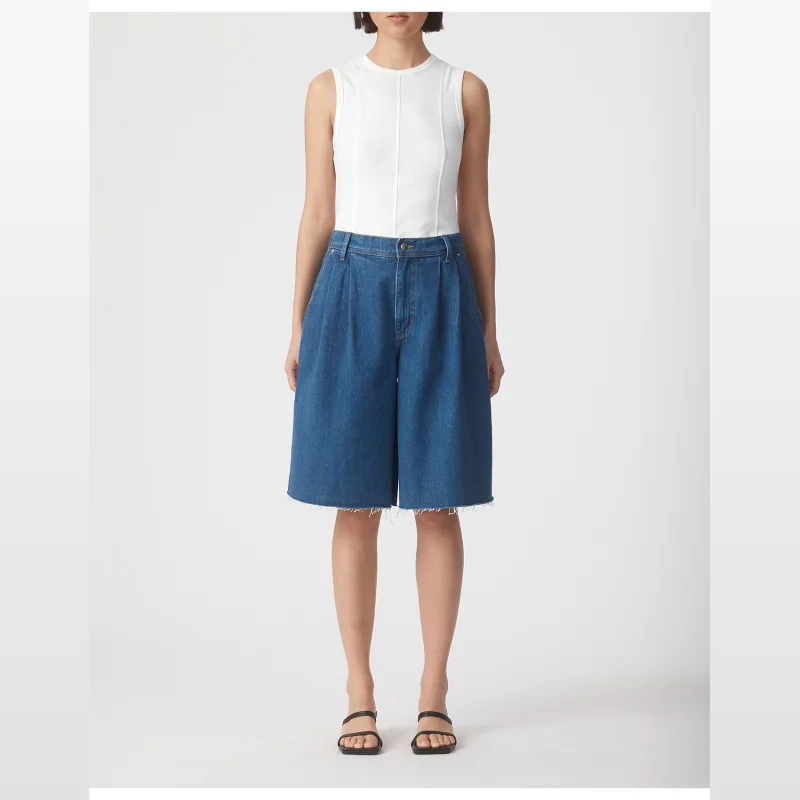 Model wearing Nobody Denim Pleat Shorts in a medium blue wash, featuring a relaxed A-line silhouette and frayed hem.
