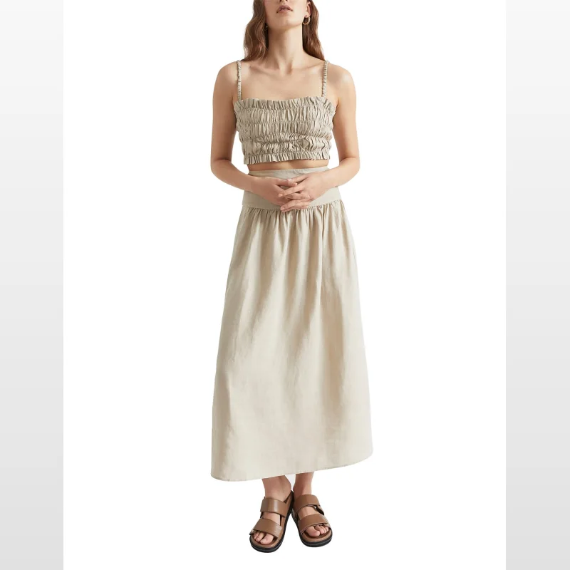 Woman wearing a beige linen ruched cropped top with thin straps and a square neckline, paired with a matching linen skirt.
