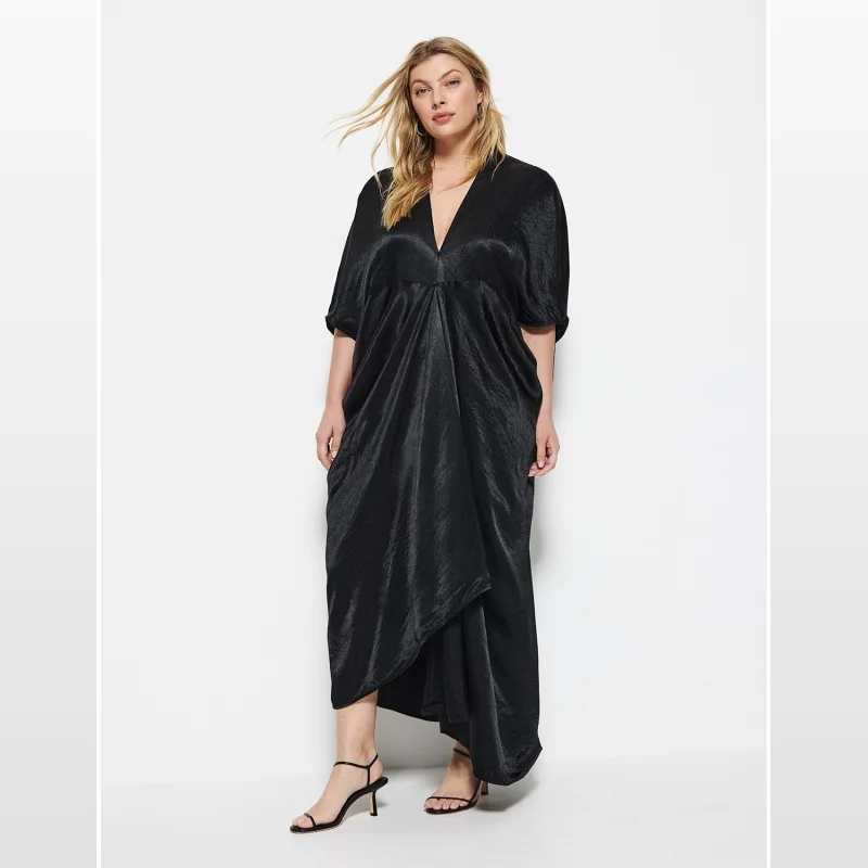 Woman wearing a black Commonry Julia Dress with a V-neckline, grown-on sleeves, and an asymmetric hemline, styled with black strappy heels.