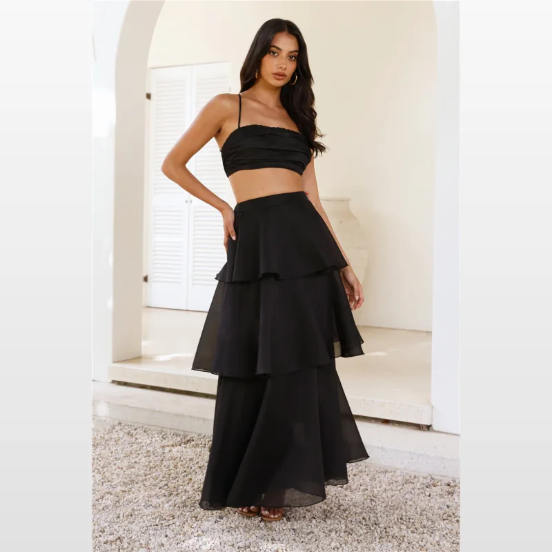 Woman wearing a black Hellomolly crop top with crisscross straps and an open back with tie, paired with a tiered black maxi skirt.